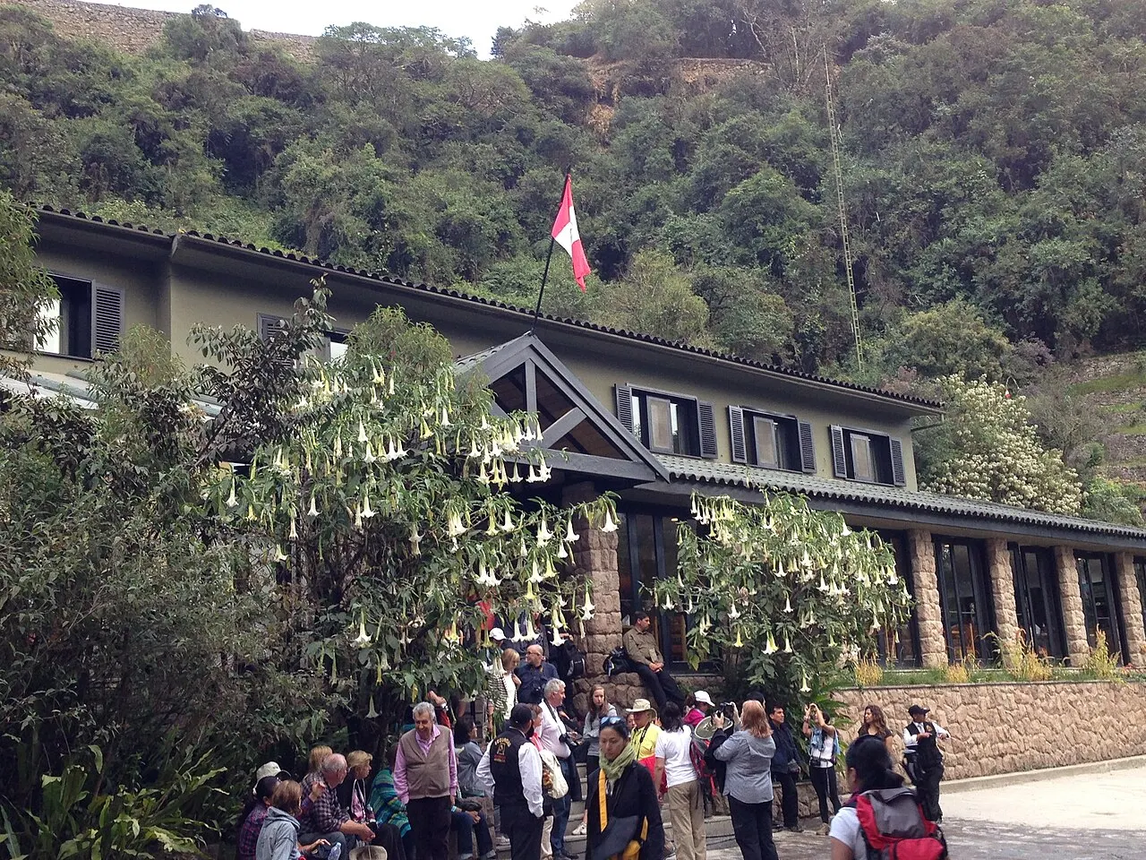 Tourists queuing for the Machu Picchu shuttle bus beside the Peruvian flag