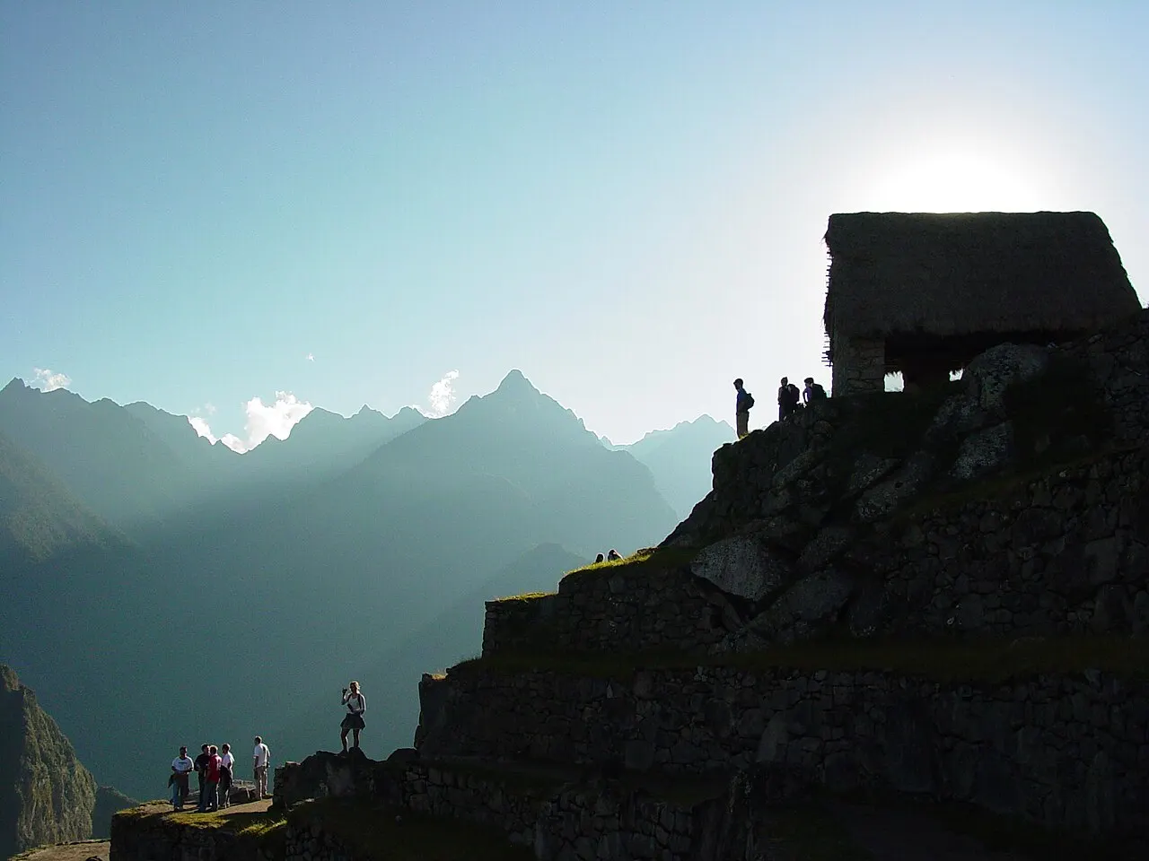 Early morning light at the Machu Picchu Guardhouse overlook with a handful of visitors and misty peaks beyond