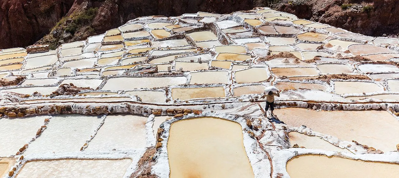 The terraced salt evaporation ponds of Maras cascading down the hillside in warm light, a worker for scale