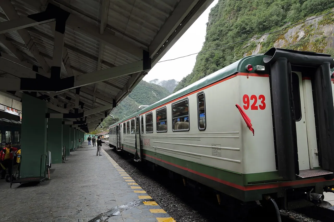 A train at the Aguas Calientes station platform beneath the steep cloud-forest walls of the gorge