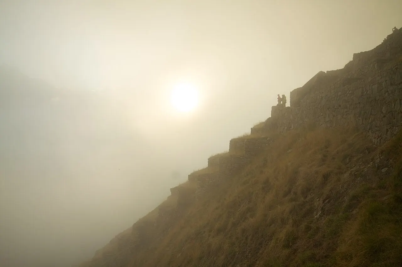 Mist-shrouded dawn over the Machu Picchu terraces with a couple of figures on the upper path
