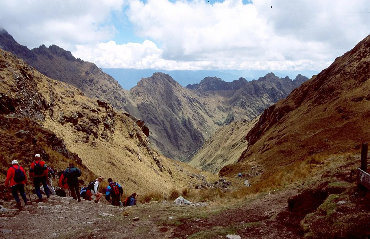 Trekkers with backpacks on the stone trail near Dead Woman's Pass on the Inca Trail, high Andean peaks ahead